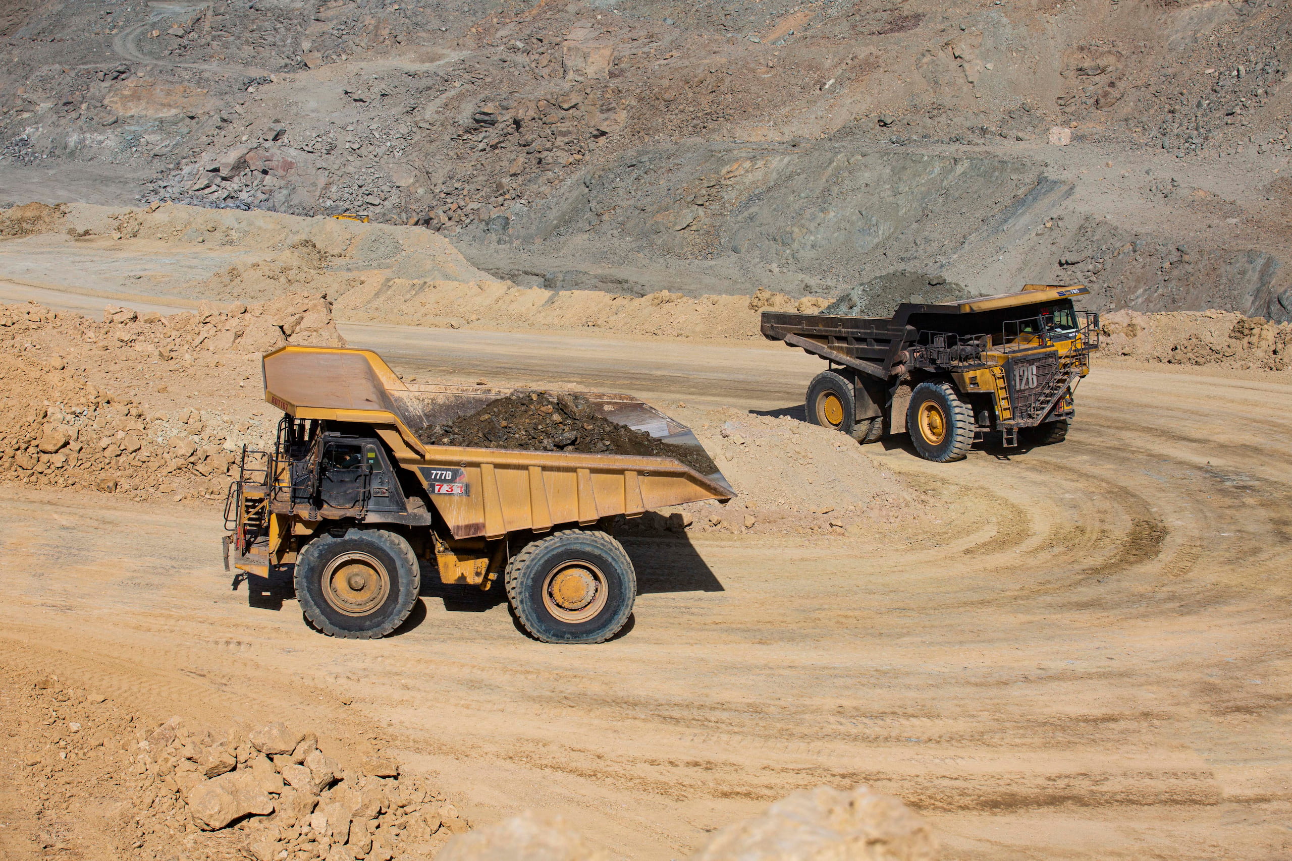Dos camiones de carga avanzan por un camino de tierra, llevando material de extracción en una zona minera.